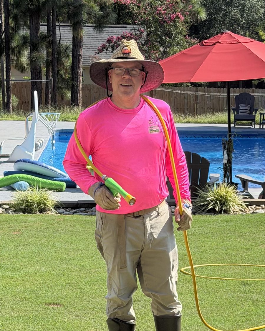 Mike Dawson, owner-operator of Flamingo Turf, in a pink Flamingo Turf shirt holding a sprayer hose